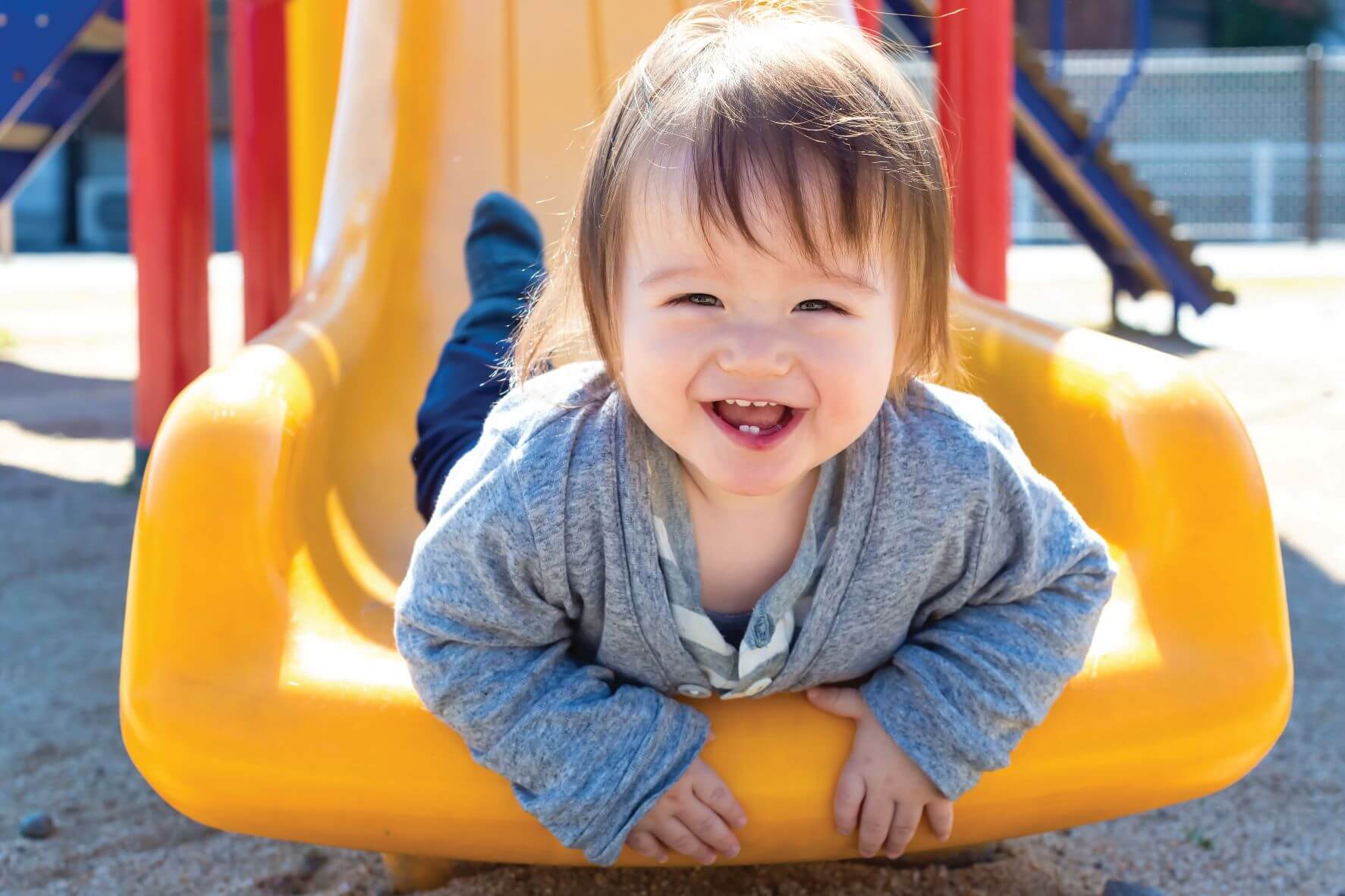 Child smiling at camera on a yellow slide